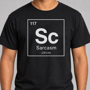 May include: A black short-sleeved t-shirt featuring a white graphic design resembling a periodic table element box. The graphic includes the number 117, the letters Sc, the word Sarcasm, and the number 293.00 enclosed in parentheses.