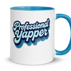 Op de afbeelding: Witte keramische mok met een blauwe binnenkant en handvat. De mok heeft de tekst "Professional Yapper" in een retro, gelaagd lettertype. Het ontwerp is in blauwtinten, waardoor een 3D-effect ontstaat.