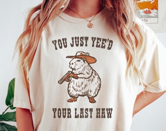 May include: A beige t-shirt with a cartoon image of a rodent wearing a cowboy hat and holding a gun. The text "You Just Yee'd Your Last Haw" is printed on the shirt.