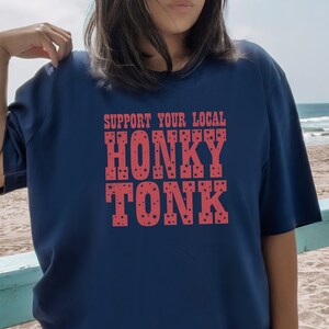 May include: A navy blue t-shirt with the text "Support Your Local Honky Tonk" in red with white stars.