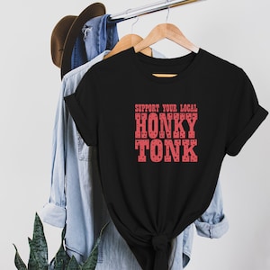 May include: Black t-shirt with a red graphic that says "Support Your Local Honky Tonk". The graphic has a polka dot pattern.