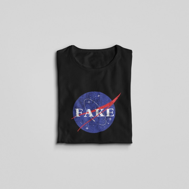 K&ouml;nnte beinhalten: Schwarzes T-Shirt mit einem blauen und roten NASA-Logo, auf dem in wei&szlig;en Buchstaben "FAKE" steht.