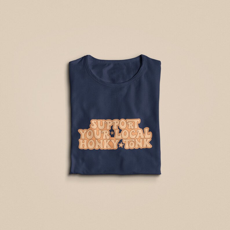 Puede incluir: Una camiseta azul marino con el texto "Support Your Local Honky Tonk" en naranja.