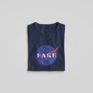 K&ouml;nnte beinhalten: Ein marineblaues T-Shirt mit einem Vintage-NASA-Logo mit dem Wort "FAKE" in wei&szlig;er Schrift.