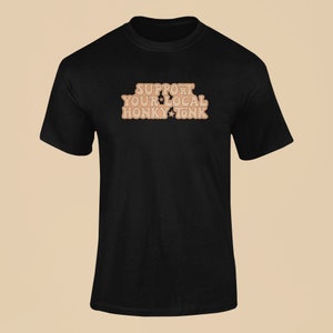 Puede incluir: Camiseta negra con el texto "Support Your Local Honky Tonk" en marr&oacute;n con estrellas.