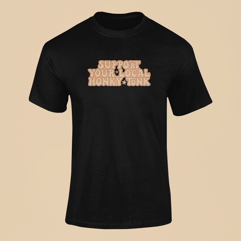 Puede incluir: Camiseta negra con el texto "Support Your Local Honky Tonk" en marr&oacute;n con estrellas.