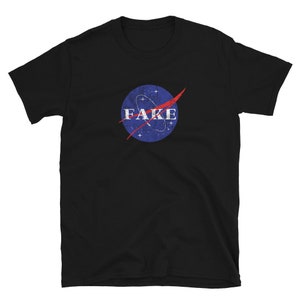 K&ouml;nnte beinhalten: Schwarzes T-Shirt mit einem blau-roten NASA-inspirierten Logo, auf dem "FAKE" in wei&szlig;er Schrift steht.