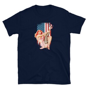 May include: A navy blue t-shirt with a vintage illustration of a woman in a pink bikini and stockings, posing in front of an American flag.