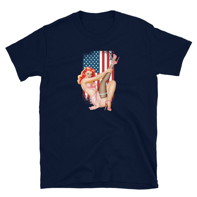 May include: A navy blue t-shirt with a vintage illustration of a woman in a pink bikini and stockings, posing in front of an American flag.