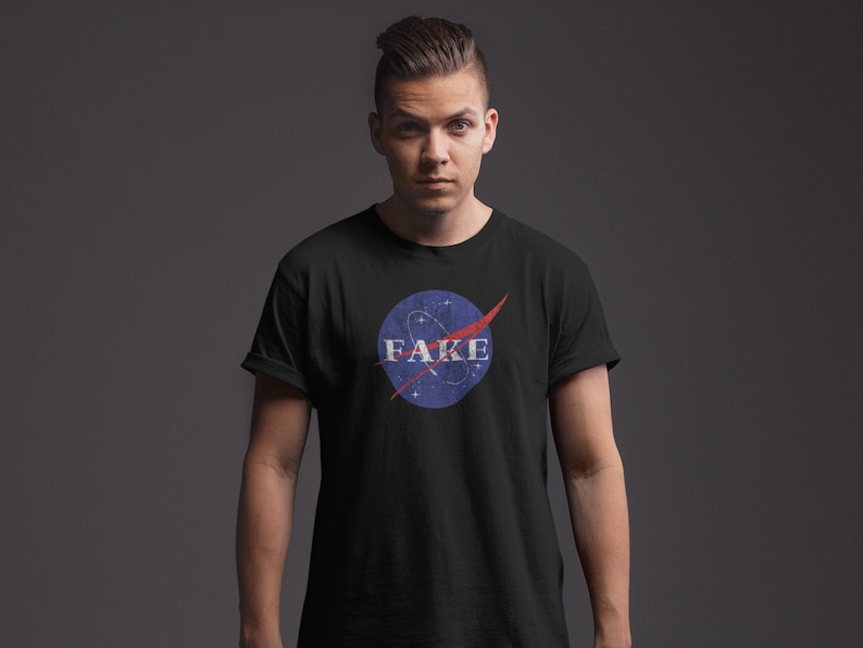 K&ouml;nnte beinhalten: Ein schwarzes T-Shirt mit einem blau-roten NASA-inspirierten Logo, auf dem in wei&szlig;en Buchstaben "FAKE" steht.
