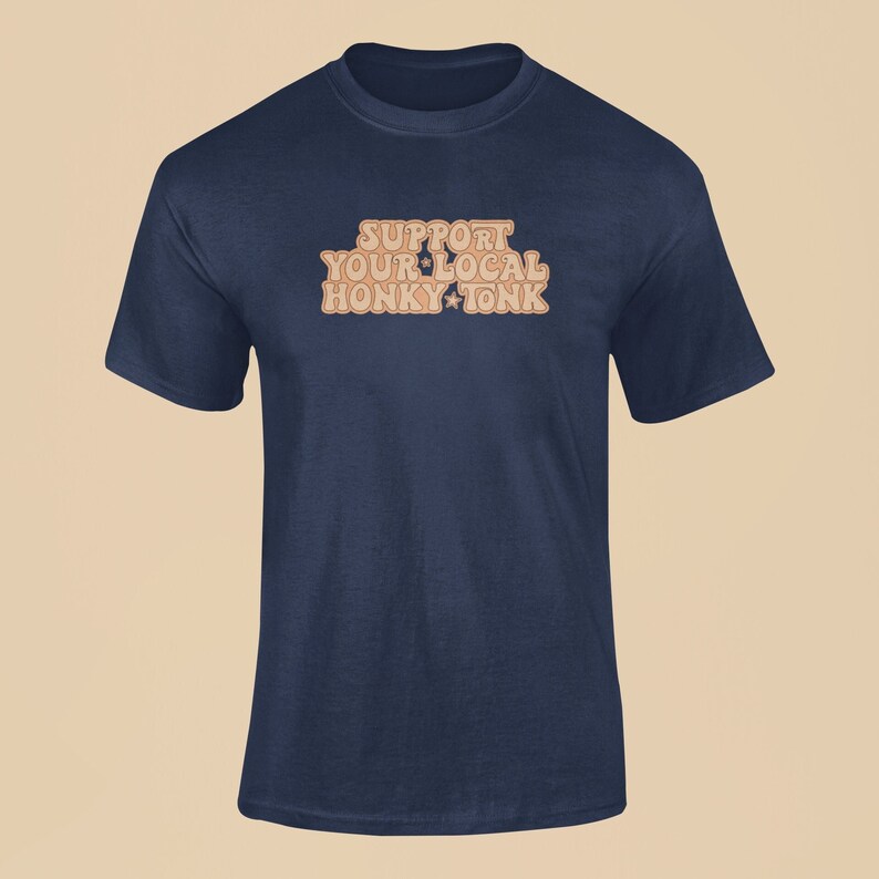 Puede incluir: Una camiseta azul marino con el texto "Support Your Local Honky Tonk" en una fuente retro con estrellas naranjas.