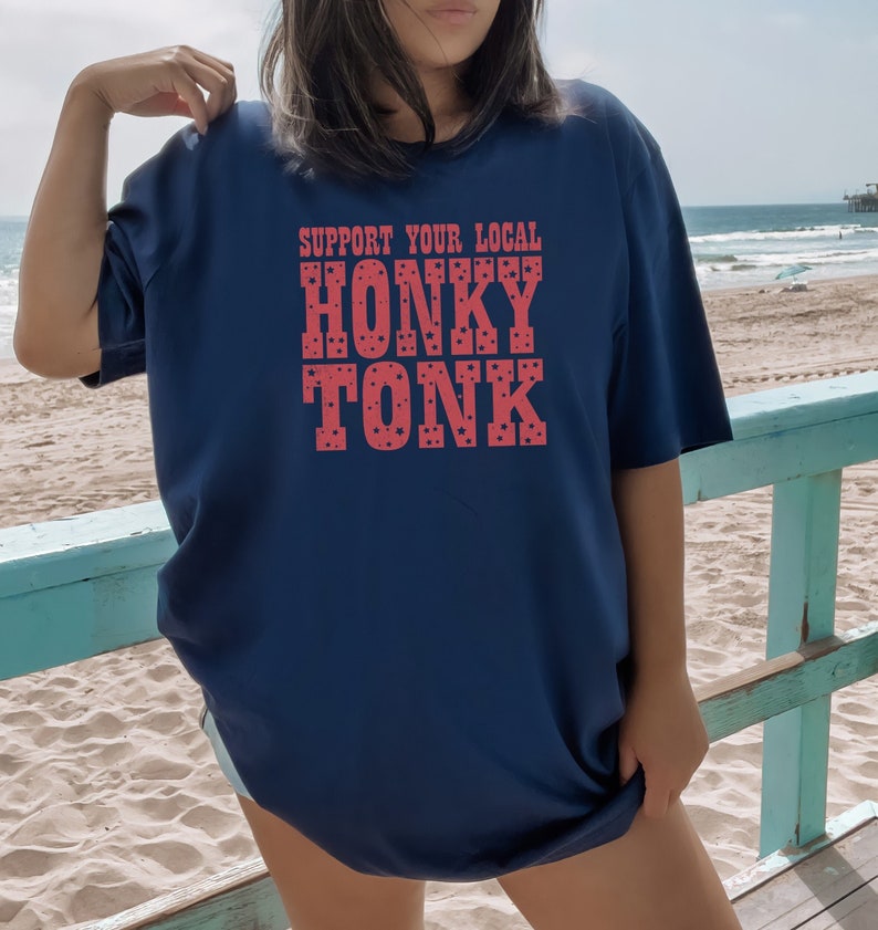 May include: A navy blue t-shirt with the text "Support Your Local Honky Tonk" in red with white stars.