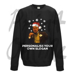 May include: Black sweatshirt featuring a white snowflake pattern and an image of Leonardo DiCaprio wearing a Santa hat and holding a glass of champagne. The text "Personalise your own slogan" is printed below the image.