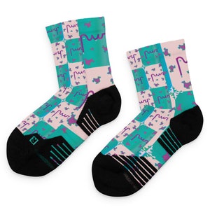 May include: A pair of athletic socks with a colorful, geometric design. The socks feature a checkerboard pattern in teal and light pink, with purple and teal abstract shapes. The cuffs and toes are black.