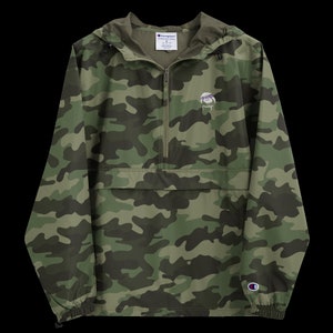 May include: A green, brown, and black camouflage print hooded jacket with a zipper closure and a small logo on the left chest. The jacket has a kangaroo pocket and elastic cuffs.