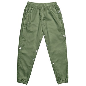 May include: Olive green track pants with an elastic waistband and pockets. The pants feature a repeating pattern of white and multi-colored embroidered designs. The fabric has a slight sheen.