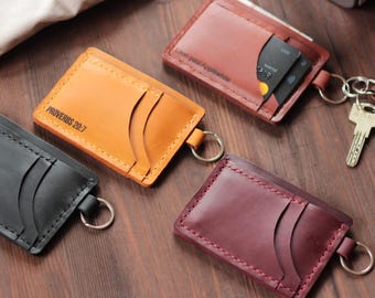 May include: Four leather cardholders in black, tan, brown, and burgundy, each with a key ring. The tan cardholder has the text "PROVERBS 20:7". The brown cardholder has the text "Leon paul Applewhite". The cardholders have slots for cards.