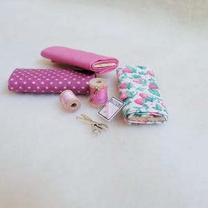 May include: A set of pink fabric scraps, two spools of pink thread, a pair of silver scissors, and a small card that says "Buttons".