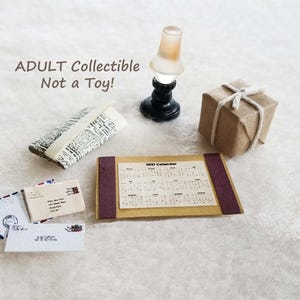 May include: A miniature set featuring a 2021 calendar, a small lamp with a black base and frosted shade, a folded newspaper, a brown paper-wrapped gift tied with white string, and three small envelopes with postage stamps and printed addresses.