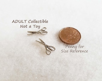 May include: Two miniature silver-toned metal scissors charms positioned next to a copper-colored Canadian penny for size reference. The text ADULT Collectible Not a Toy and Penny for Size Reference is printed on the image near the items.
