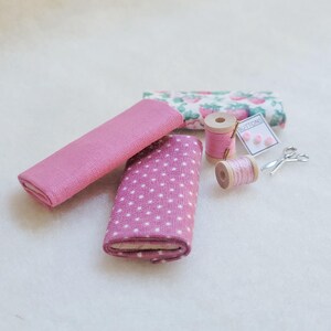 May include: A set of pink fabric scraps, two spools of pink thread, a small package of buttons labeled "Buttons", and a pair of silver scissors.