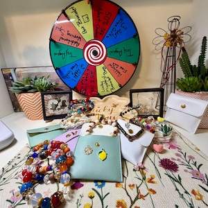 May include: A colorful display of jewelry and accessories, including bracelets, small pouches, and a prize wheel. The bracelets feature various beads in shades of red, blue, orange, and white. The prize wheel has text such as "50% Off" and "Free Gifts".