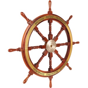 Puede incluir: Un gran timón de barco de madera con ocho radios y un borde de latón. El timón está inscrito con las palabras "Browns Patent Telemotor Rosebank Ironworks Edinburgh".