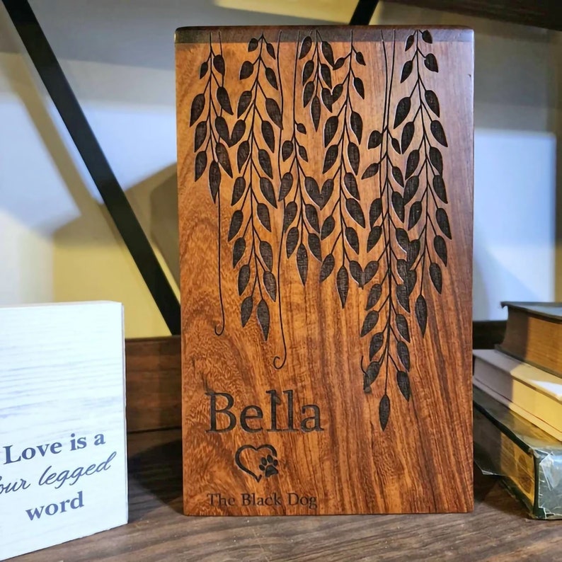 May include: A wooden box with a carved design of weeping willow branches. The box is engraved with the name "Bella" and the text "The Black Dog".