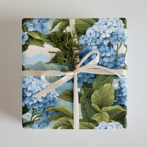 Puede incluir: Una caja de regalo envuelta en papel con estampado floral azul y verde con una cinta blanca y una rama de vegetación.