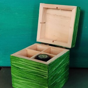 Peut inclure: Une boîte en bois verte avec quatre compartiments, dont l'un contient une petite montre ronde. La boîte a un motif de grain de bois et est ouverte.