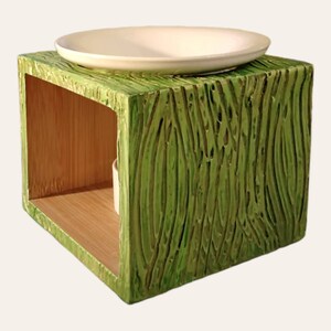 Peut inclure: Diffuseur d'huiles essentielles en céramique verte avec un plat en céramique blanche sur le dessus. Le diffuseur a une texture en bois et une forme carrée.