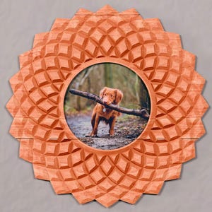 May include: A circular wooden picture frame with a carved, geometric, sunburst-like pattern on the outer edge. The frame contains a photograph of a golden-coloured dog standing in a wooded area while holding a dark wooden stick in its mouth.