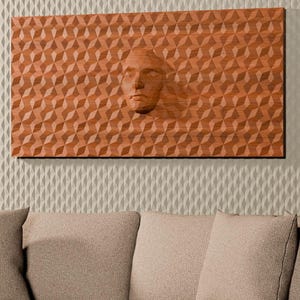 May include: A rectangular terracotta-colored wall panel featuring a repeating geometric triangular pattern and a central human face relief. The panel is mounted on a textured off-white wall flanked by vertical wood slat panels on both sides.