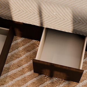 May include: A dark brown wooden bed frame featuring two open storage drawers positioned underneath the base. The drawers have light-coloured interiors and are integrated into the frame, which is partially covered by a textured beige fabric.