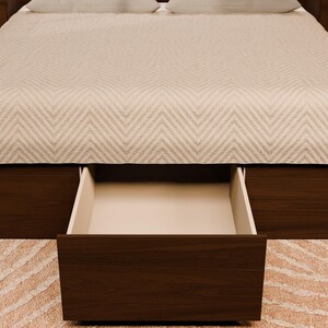 May include: A dark brown wooden bed frame featuring a large, open storage drawer at the base. The bed is covered with a light-coloured, chevron-patterned quilt. The frame includes integrated side panels that extend to form matching bedside tables.