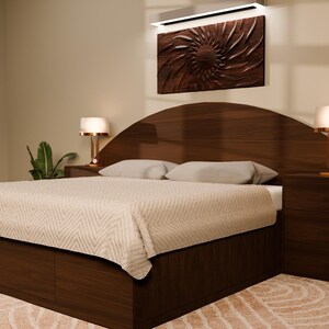 May include: A dark wood bed frame featuring a large, arched headboard with integrated side tables and two lamps. The bed is dressed in a light-coloured, textured quilt with two matching pillows. Above the headboard hangs a dark, circular wall art piece.