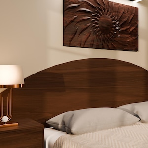 May include: A dark wood arched headboard with matching bedside tables, each featuring a gold-toned lamp with a white cylindrical shade. A textured white bedspread with two pillows sits in front of the headboard, beneath a dark wood wall art piece.