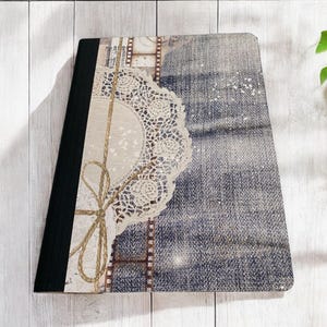 May include: A notebook with a denim-like cover featuring a lace doily and a brown twine bow. The cover also has a vintage film strip design.