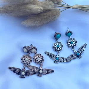 May include: A pair of silver tone dangle earrings with turquoise and white stones. The earrings feature a flower design with a bird pendant.