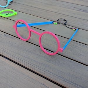 May include: A pair of pink plastic round glasses with blue arms and a black cord.