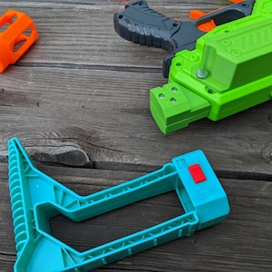 May include: A green and black toy gun with a blue and red plastic stock. The gun has a textured surface and a black handle. The stock has a red button on the side.