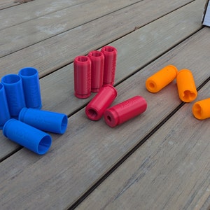 May include: A group of blue, red, and orange plastic toy bullets. The blue bullets are arranged in a semi-circle, the red bullets are scattered, and the orange bullets are in a pile.