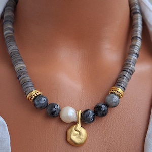May include: A necklace featuring a strand of gray, disc-shaped beads. The necklace has a section of faceted gray beads, a white pearl, and a gold-colored pendant. Gold-colored spacers are between the beads.