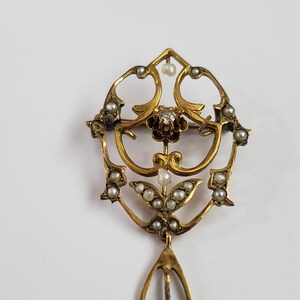 May include: A gold pendant with a delicate, intricate design featuring a central diamond and pearl accents. The pendant is suspended from a long, thin chain.
