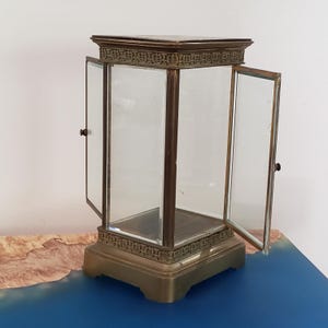 K&ouml;nnte beinhalten: Eine Vitrine aus Messing mit Glast&uuml;ren und quadratischem Sockel. Die T&uuml;ren sind ge&ouml;ffnet und die Vitrine ist leer.