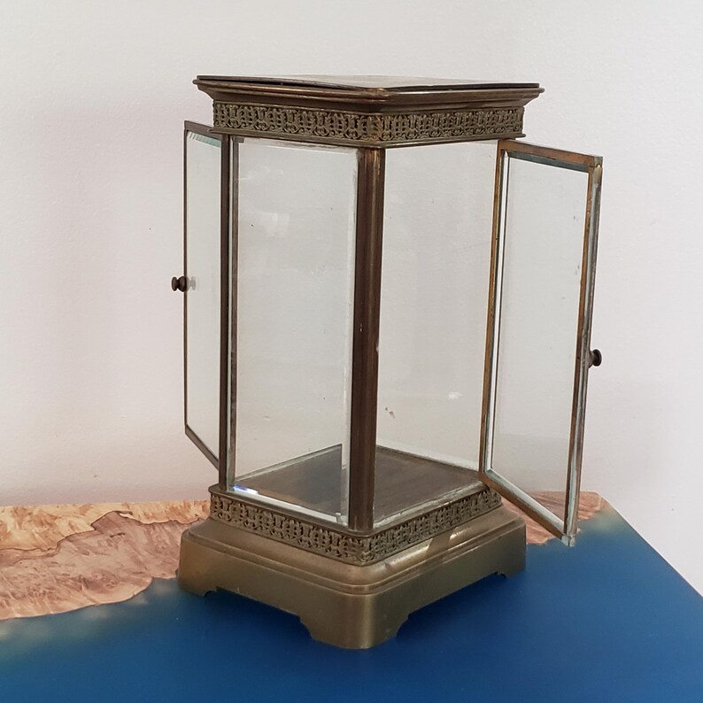 K&ouml;nnte beinhalten: Eine Vitrine aus Messing mit Glast&uuml;ren und quadratischem Sockel. Die T&uuml;ren sind ge&ouml;ffnet und die Vitrine ist leer.