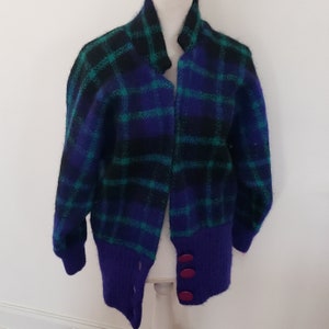 May include: A blue, green, and black plaid cardigan with a purple trim and three red buttons.