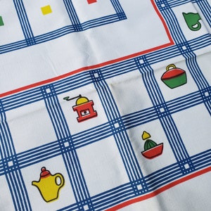May include: A white tablecloth with a blue and red checkered pattern. The tablecloth features various kitchen-themed illustrations, including a coffee grinder, a teapot, a lemon, and a sugar bowl.