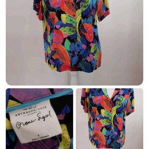 May include: A short-sleeved, button-up shirt with a colorful tropical fruit print. The shirt is black with bright orange, yellow, green, and blue fruits. The label reads "The Art of Anthropologie featuring  " and "Grome Siegel".