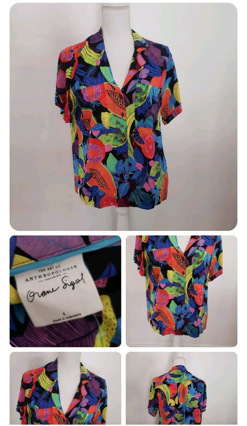 May include: A short-sleeved, button-up shirt with a colorful tropical fruit print. The shirt is black with bright orange, yellow, green, and blue fruits. The label reads "The Art of Anthropologie featuring  " and "Grome Siegel".